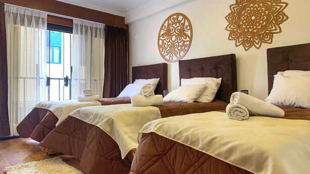 A hotel room with three beds, each with brown headboards and white linens. There are decorative wall hangings above the beds. - Del Niño Apartments (Cusco)