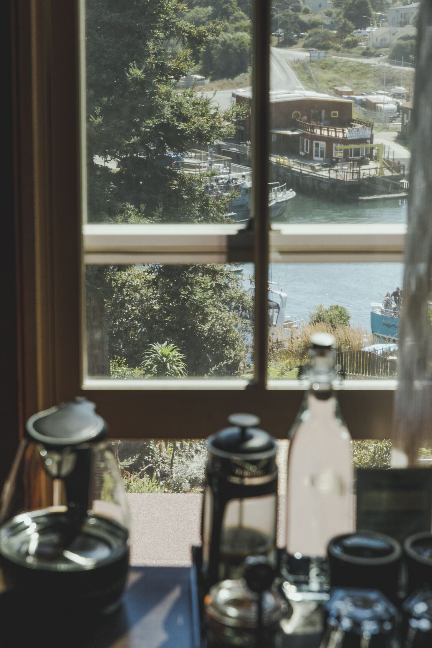 Une vue à travers une fenêtre, avec une machine à café et une bouteille posées sur une table.