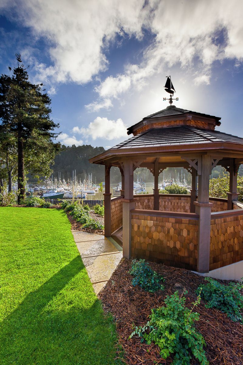 A gazebo with a weather vane, surrounded by a well-maintained lawn and a view of boats in the distance.