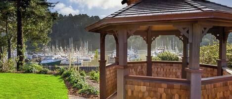 A gazebo with a weather vane, surrounded by a well-maintained lawn and a view of boats in the distance.
