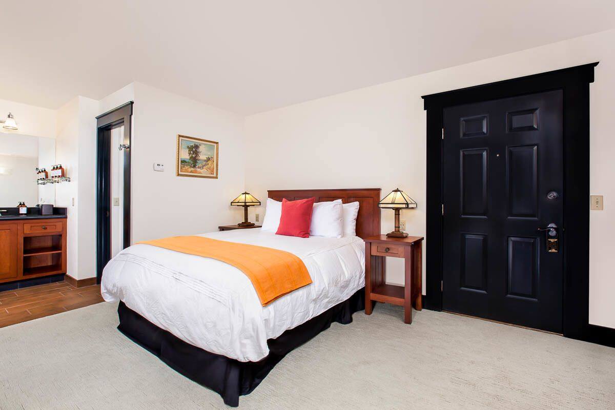 A hotel room with a large bed, a wooden dresser, a desk, and a black door.