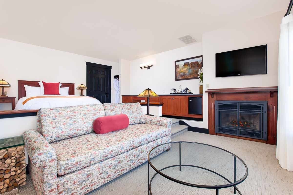 A hotel room with a bed, a sofa, a TV, a fireplace, and a dining area.