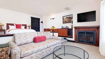 A hotel room with a bed, a sofa, a TV, a fireplace, and a dining area.