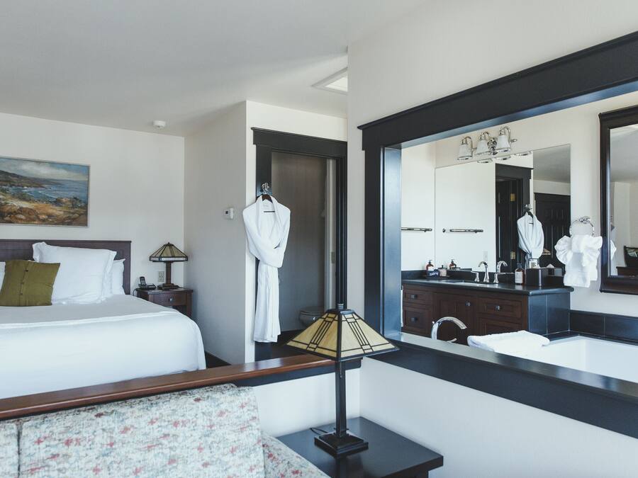 Une chambre d’hôtel comprenant un lit, une table de chevet, une lampe, un miroir et une salle de bain avec un lavabo et un miroir.