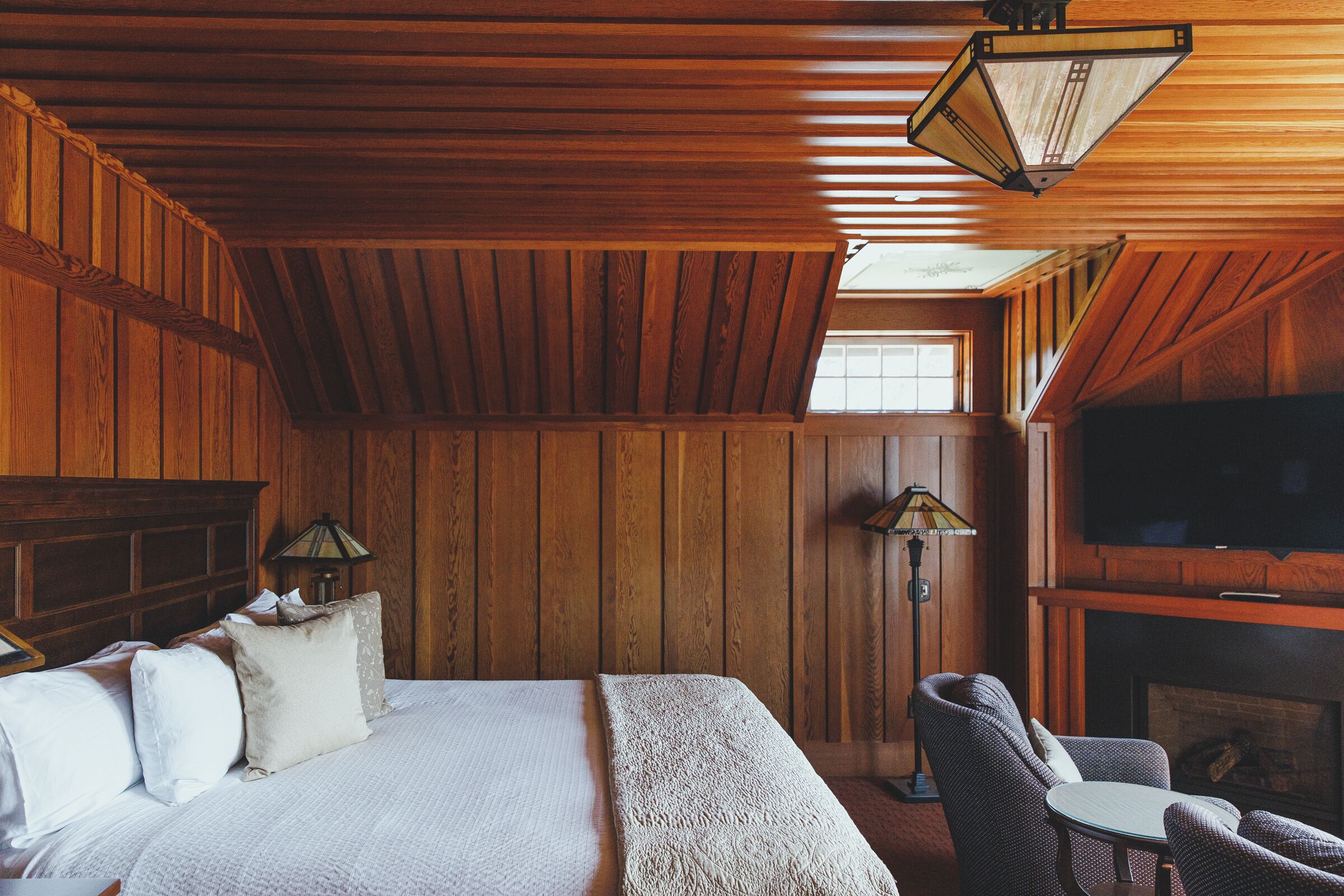 Ein Zimmer mit Holzwänden, einem Bett, einem Kamin und einem Fernseher.
