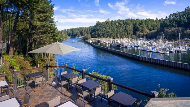 A riverside patio with tables and chairs, overlooking a marina with boats. - Noyo Harbor Inn Restaurant and Tavern (Fort Bragg)