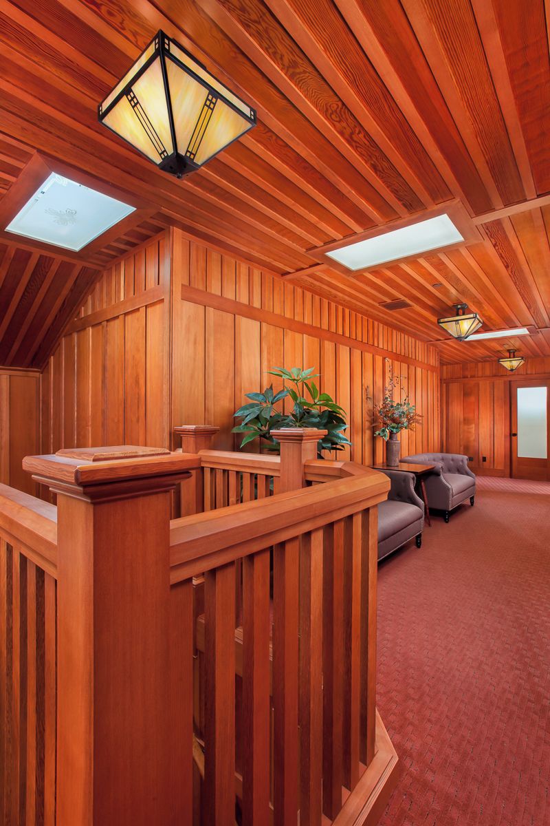 A wooden interior with a sloped ceiling, a wooden railing, and two potted plants.