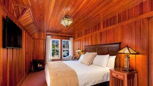 A wooden-paneled bedroom with a large bed, two bedside lamps, and a fireplace. - Noyo Harbor Inn Restaurant and Tavern (Fort Bragg)