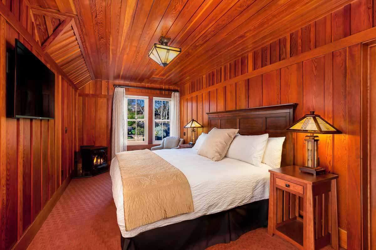 A wooden-paneled bedroom with a large bed, two bedside lamps, and a fireplace.