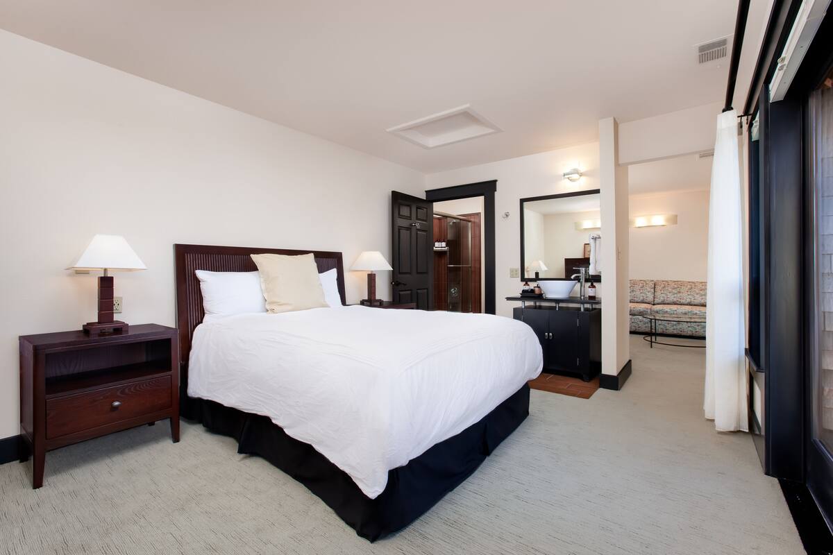 A hotel room with a large bed, bedside tables, a desk, and a sofa.