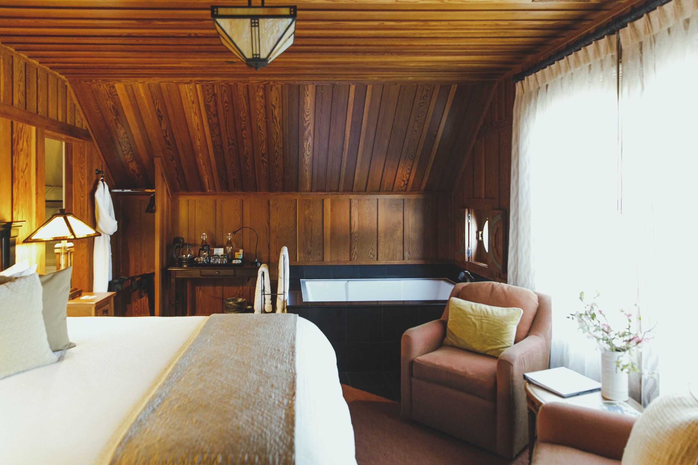 A wooden-paneled room with a bed, a chair, a desk, and a window.