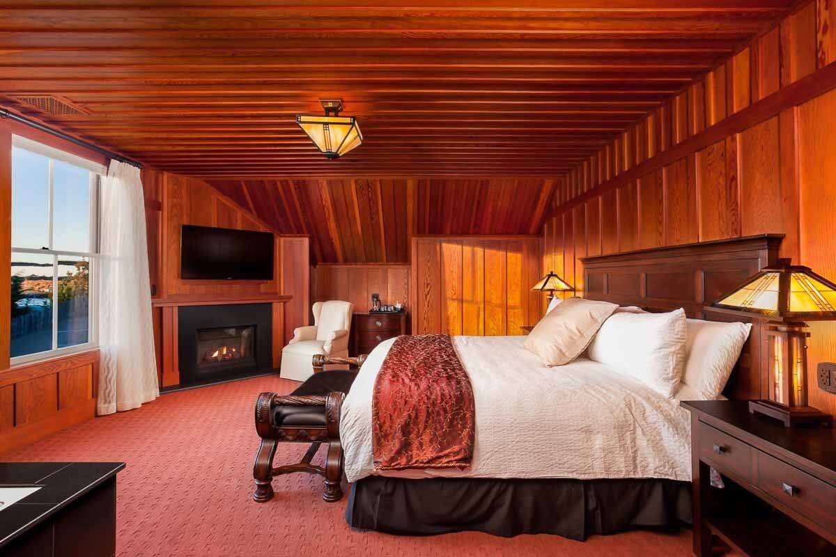 A wooden-paneled room with a bed, a fireplace, a television, and a desk.