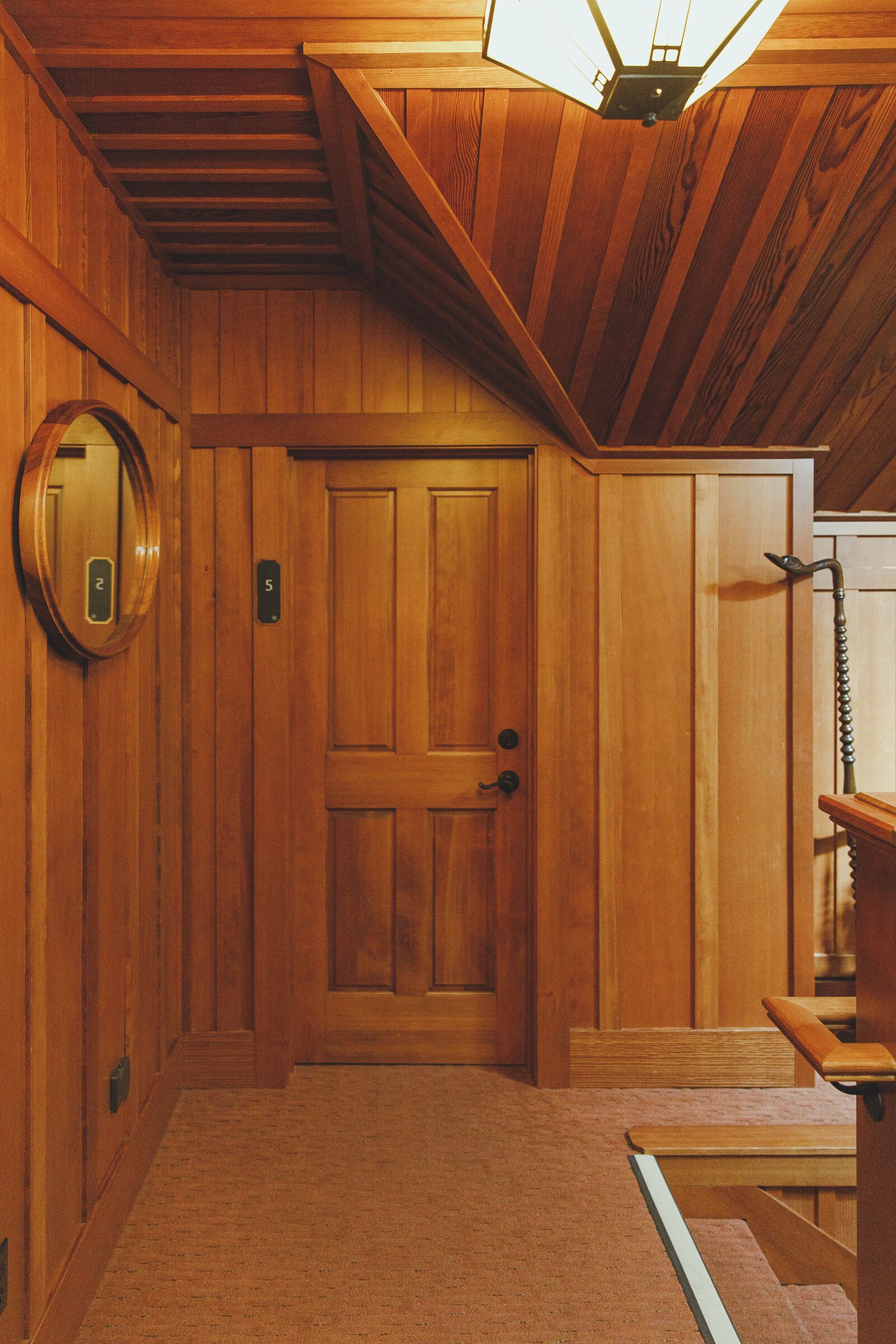 A wooden interior hallway with a door, a wall-mounted elevator, and a bench.