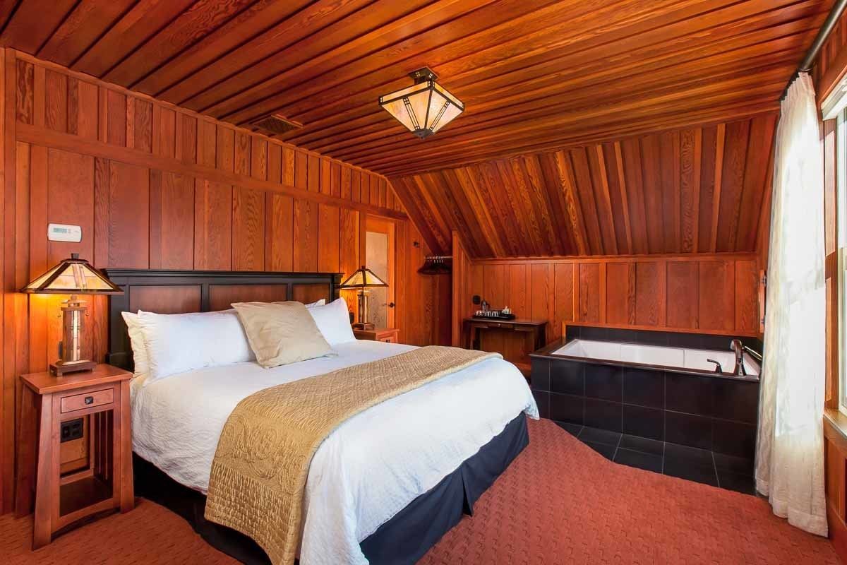 Dormitorio con paneles de madera, cama, lámparas de noche, mesita de noche y bañera.