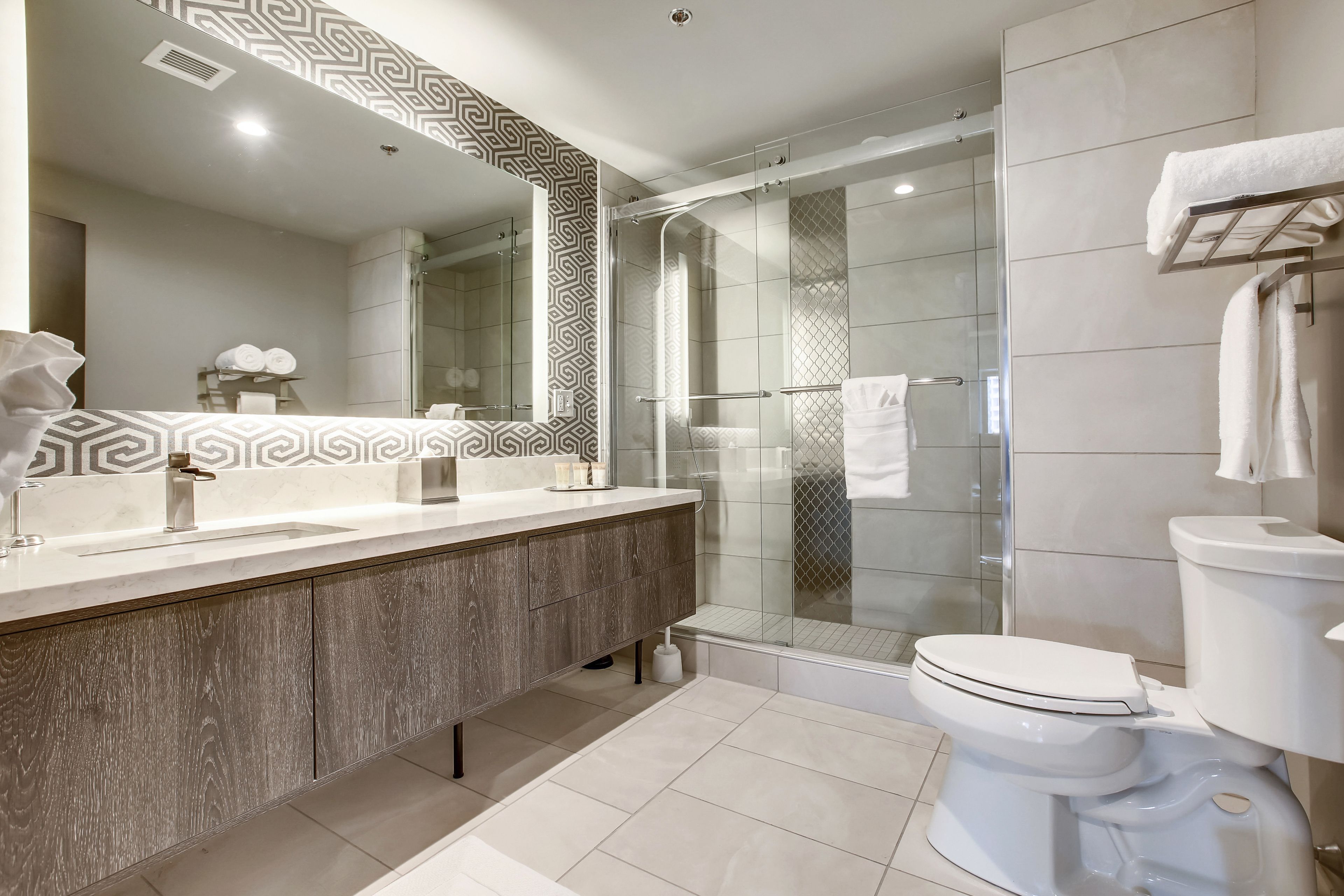 Un baño moderno con un espejo grande, un tocador con lavamanos, cabina de ducha y retrete.