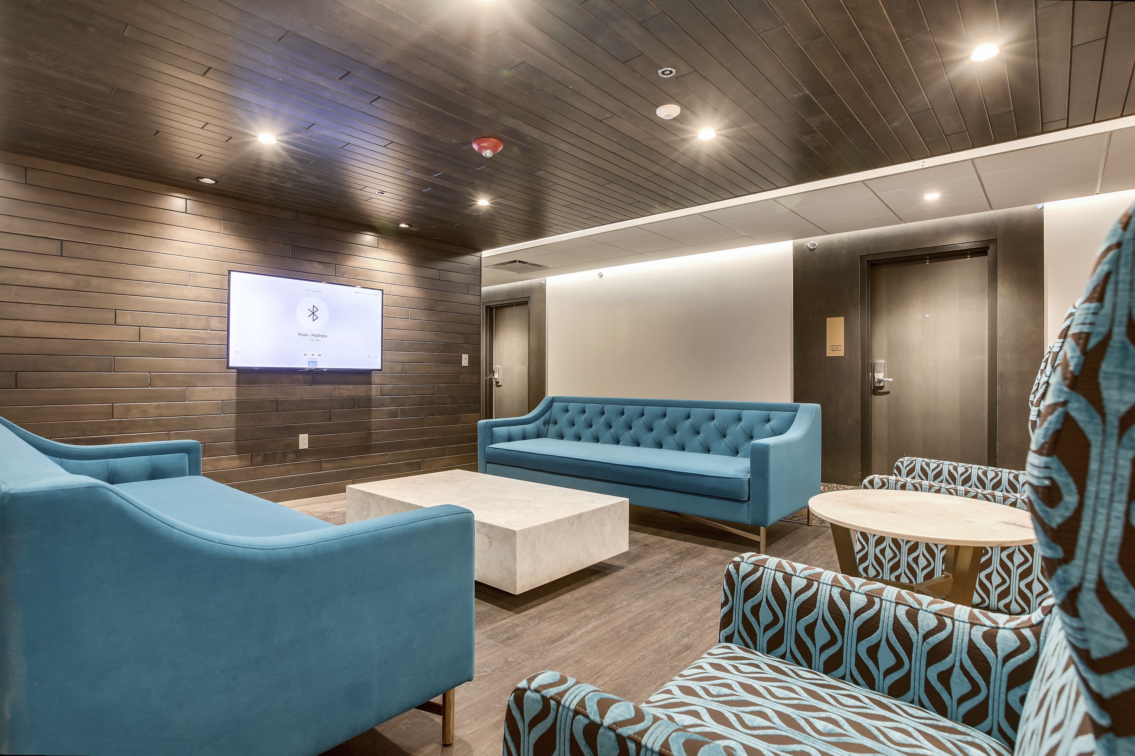Un salon moderne avec un canapé bleu, des fauteuils à motifs et un téléviseur à écran plat fixé au mur.