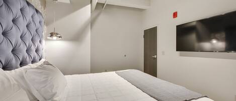 A bedroom with a large bed, a television mounted on the wall, and a door in the background.