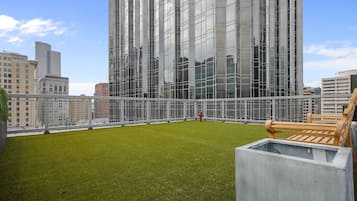 Terraço no telhado com grama sintética, um hidrante e um banco de madeira.