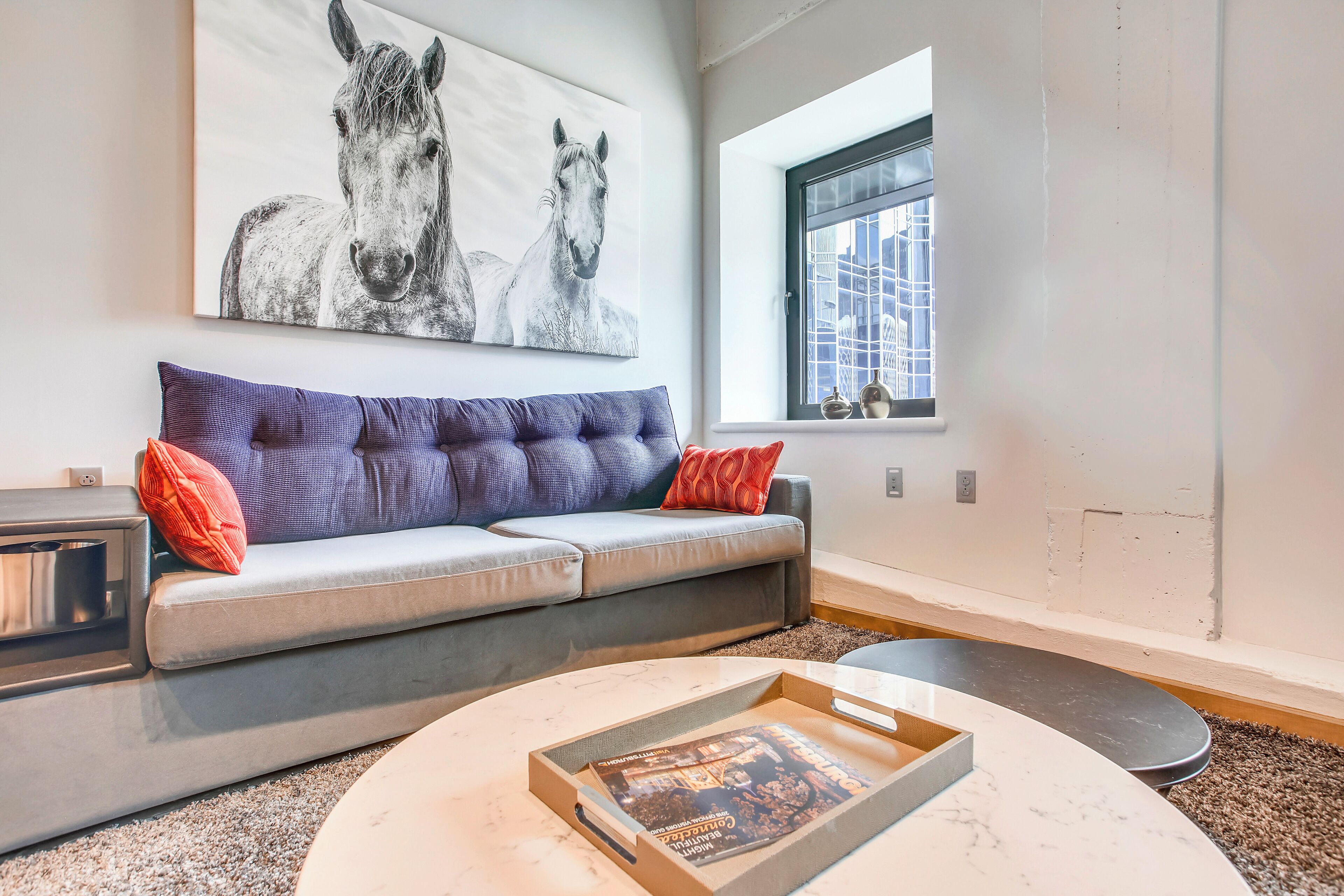 A modern living room with a grey sofa, a coffee table, and a large horse painting on the wall.