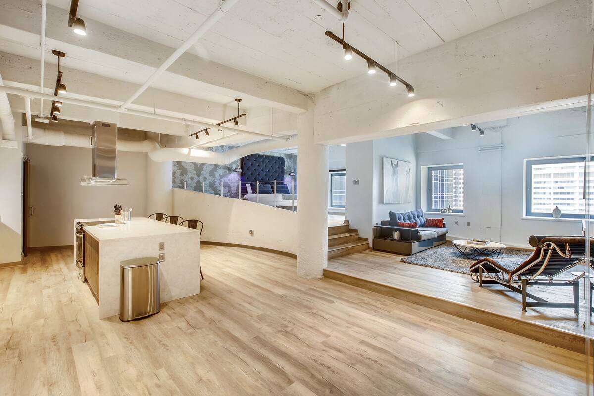 A spacious living area with a kitchen island, a dining area, and a seating area with a sofa and lounge chair.