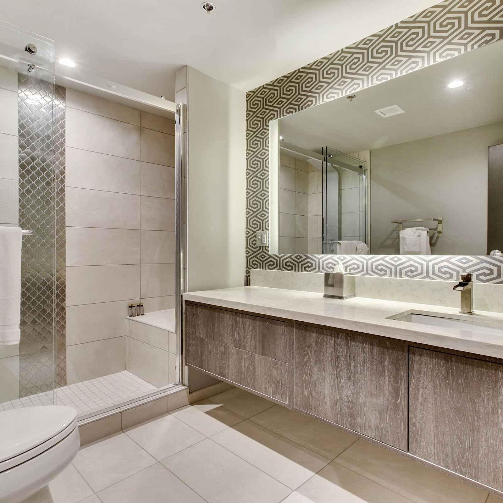 Un bagno moderno con box doccia in vetro, uno specchio grande e un mobile bagno in legno.