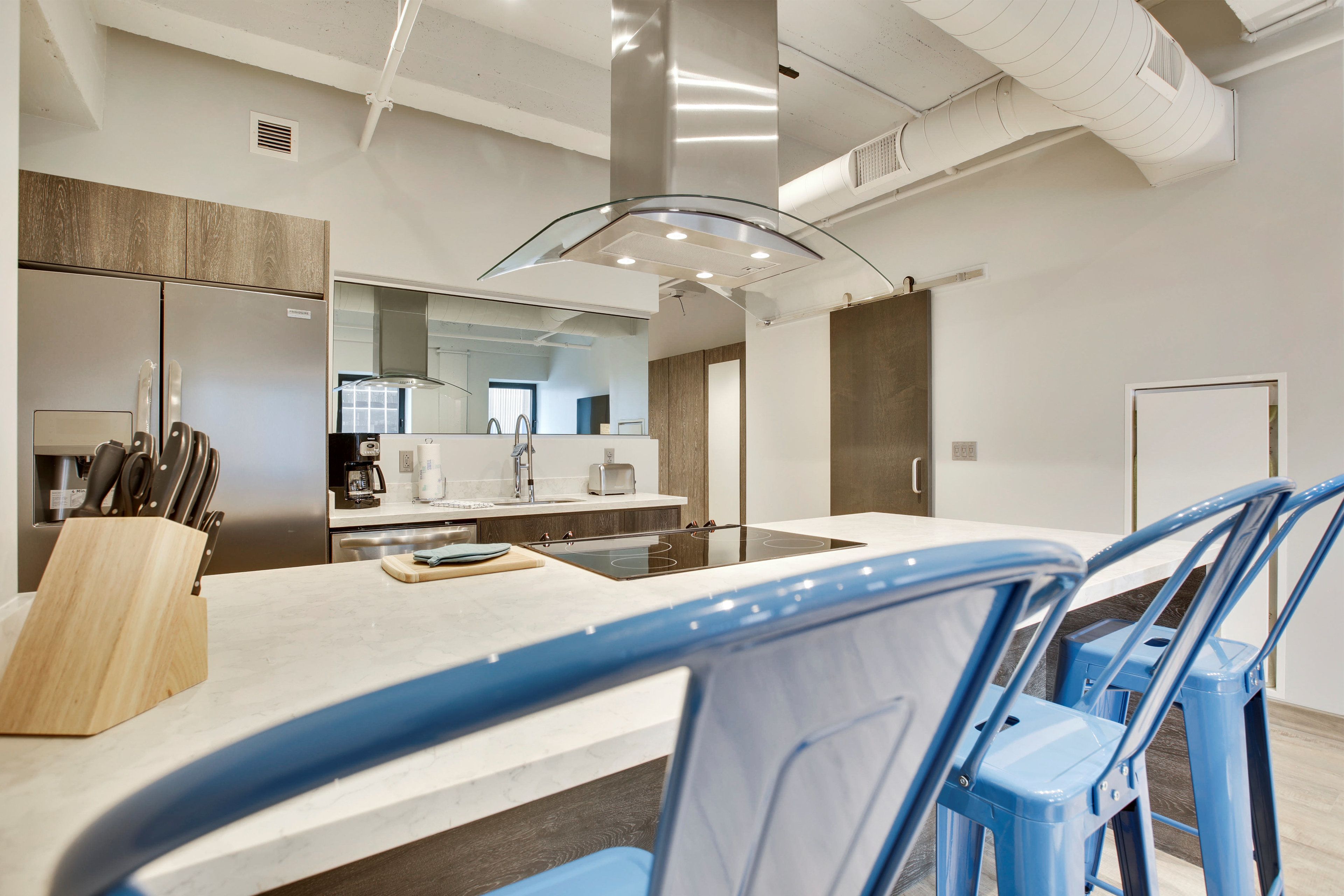 A modern kitchen with a central island, stainless steel appliances, and blue chairs.