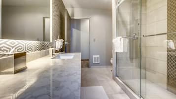 A modern bathroom with a glass-enclosed shower, a marble vanity, and patterned wall tiles.