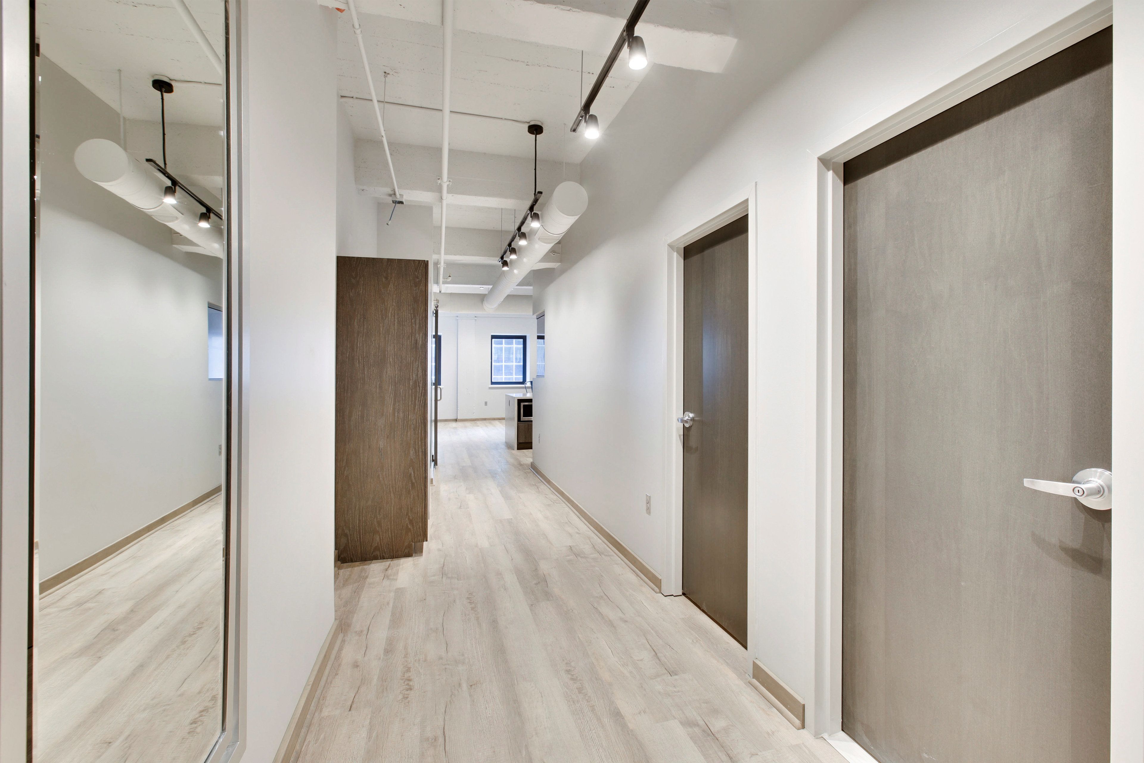 A corridor with wooden flooring, white walls, and a door on the right.