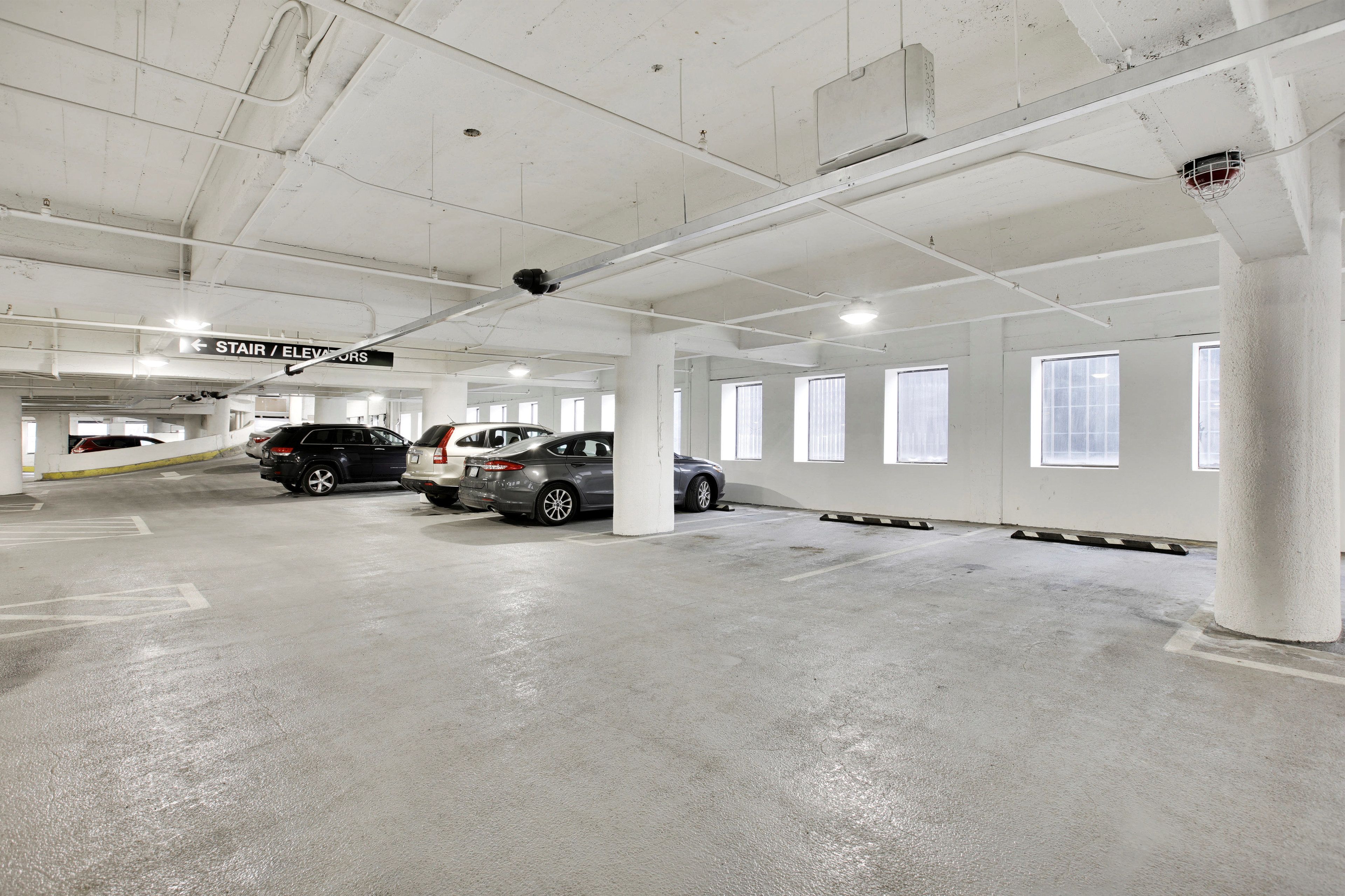A parking garage with white pillars, clear signage for elevators, and multiple parked cars.