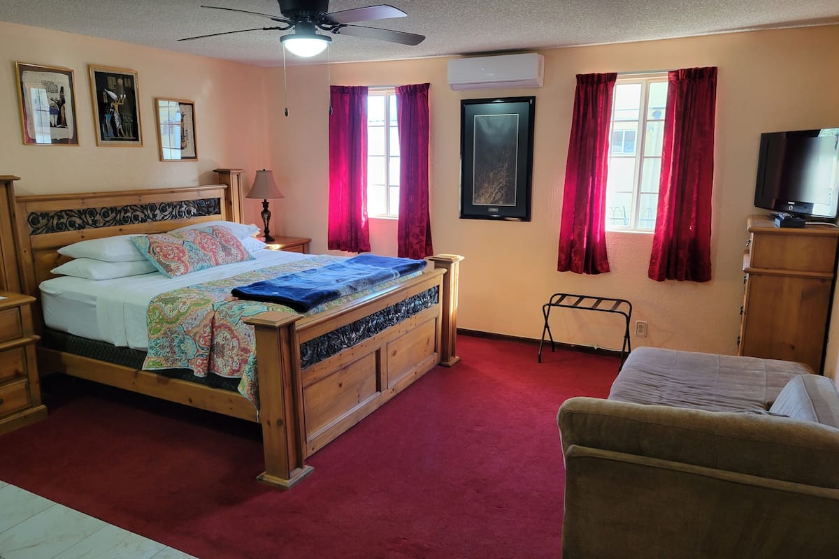 A bedroom with a wooden bed, a ceiling fan, a TV, and a window with red curtains.