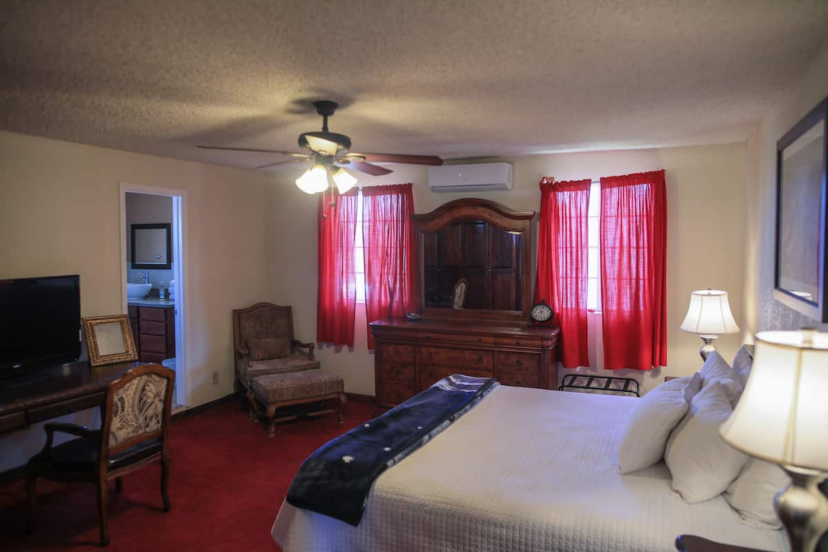 A hotel room with a bed, a desk with a television, a chair, a dresser, and a ceiling fan.