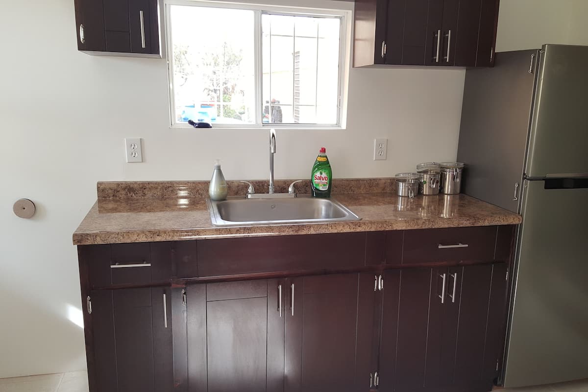 A kitchen with dark wooden cabinets, a stainless steel sink, a refrigerator, and a window with blinds.