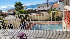 Zona de piscina con vista al océano, baranda blanca y un taburete morado.