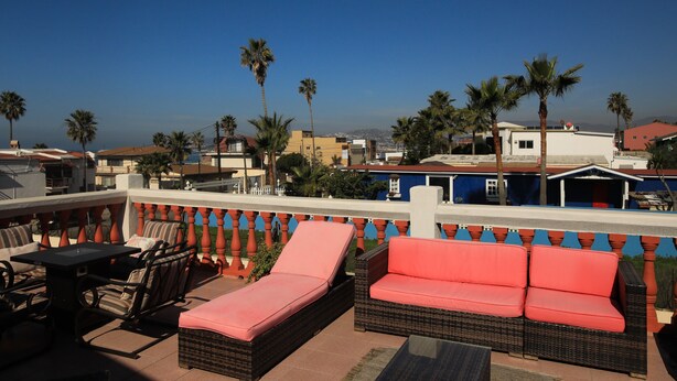 Una terraza en la azotea con mobiliario de mimbre, una mesa y vistas de la ciudad.