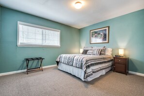 Een slaapkamer met een bed, nachtkastje, lamp en een raam met jaloezieën.