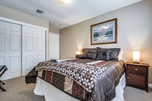 Een slaapkamer met een groot bed, een nachtkastje, een ingelijst beeld aan de muur en een kast.