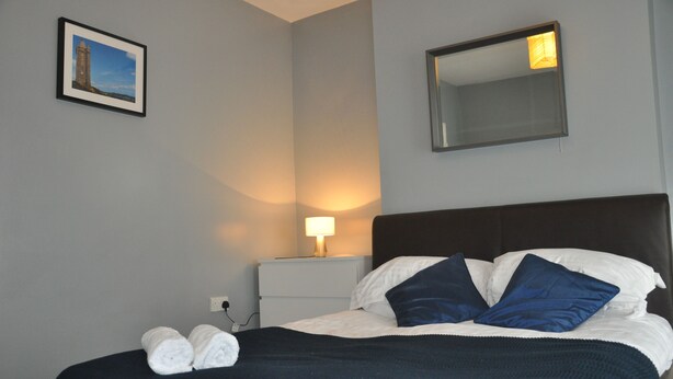A neatly made bed with white and blue pillows, a dark headboard, and a bedside lamp.