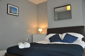 A neatly made bed with white and blue pillows, a dark headboard, and a bedside lamp. - Top Of The Town House (Bangor)