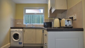 A compact kitchen with a washing machine, a toaster, and a window with blinds.
