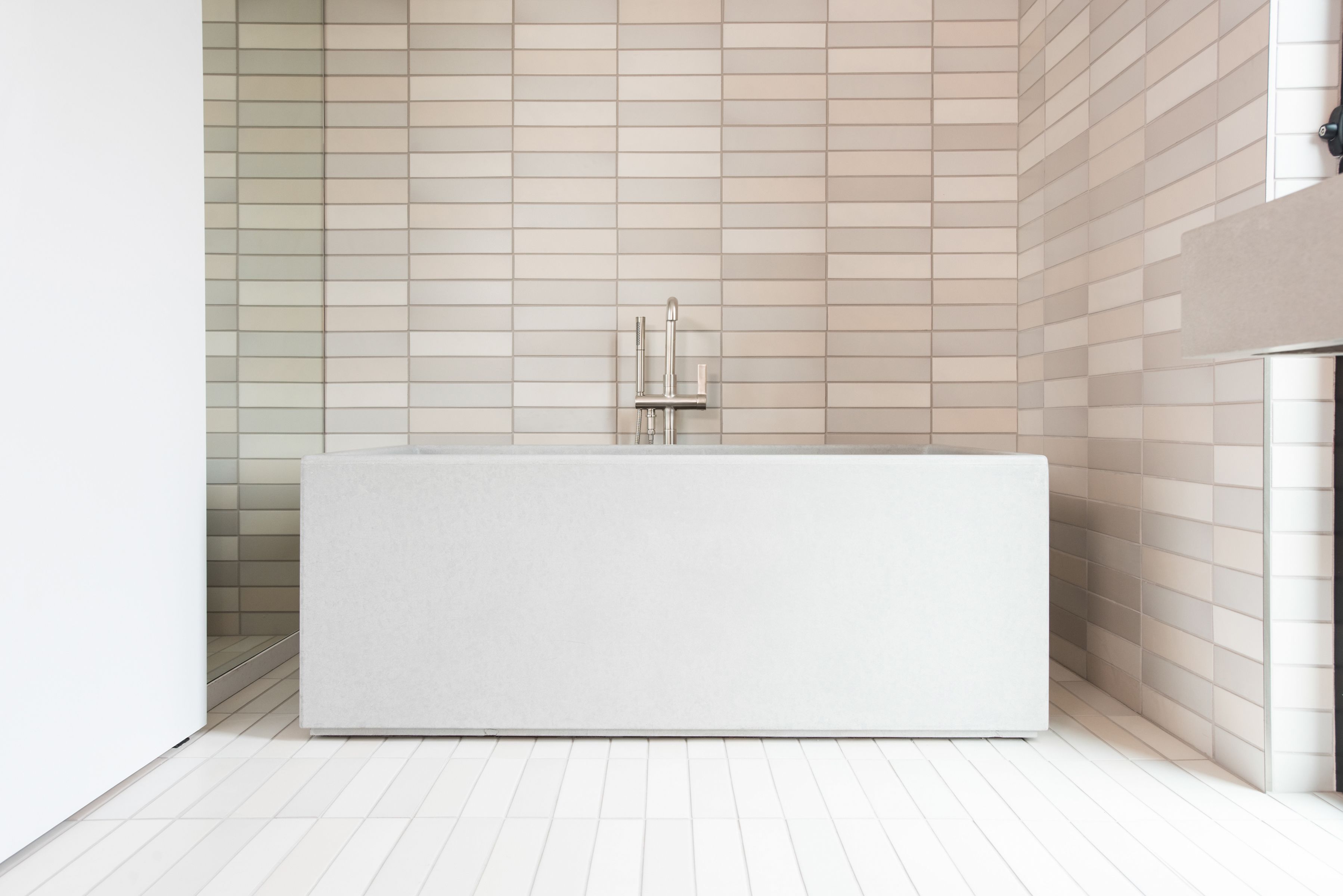 A modern bathroom with a large rectangular bathtub, a wall-mounted faucet, and a tiled floor.