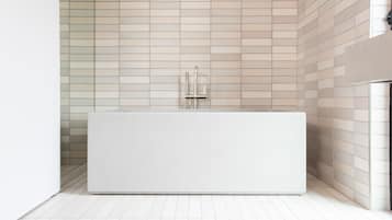 A modern bathroom with a large rectangular bathtub, a wall-mounted faucet, and a tiled floor.