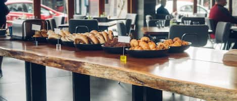 Un bufé de desayuno con diversos pasteles y productos de panadería exhibidos en una barra de madera.