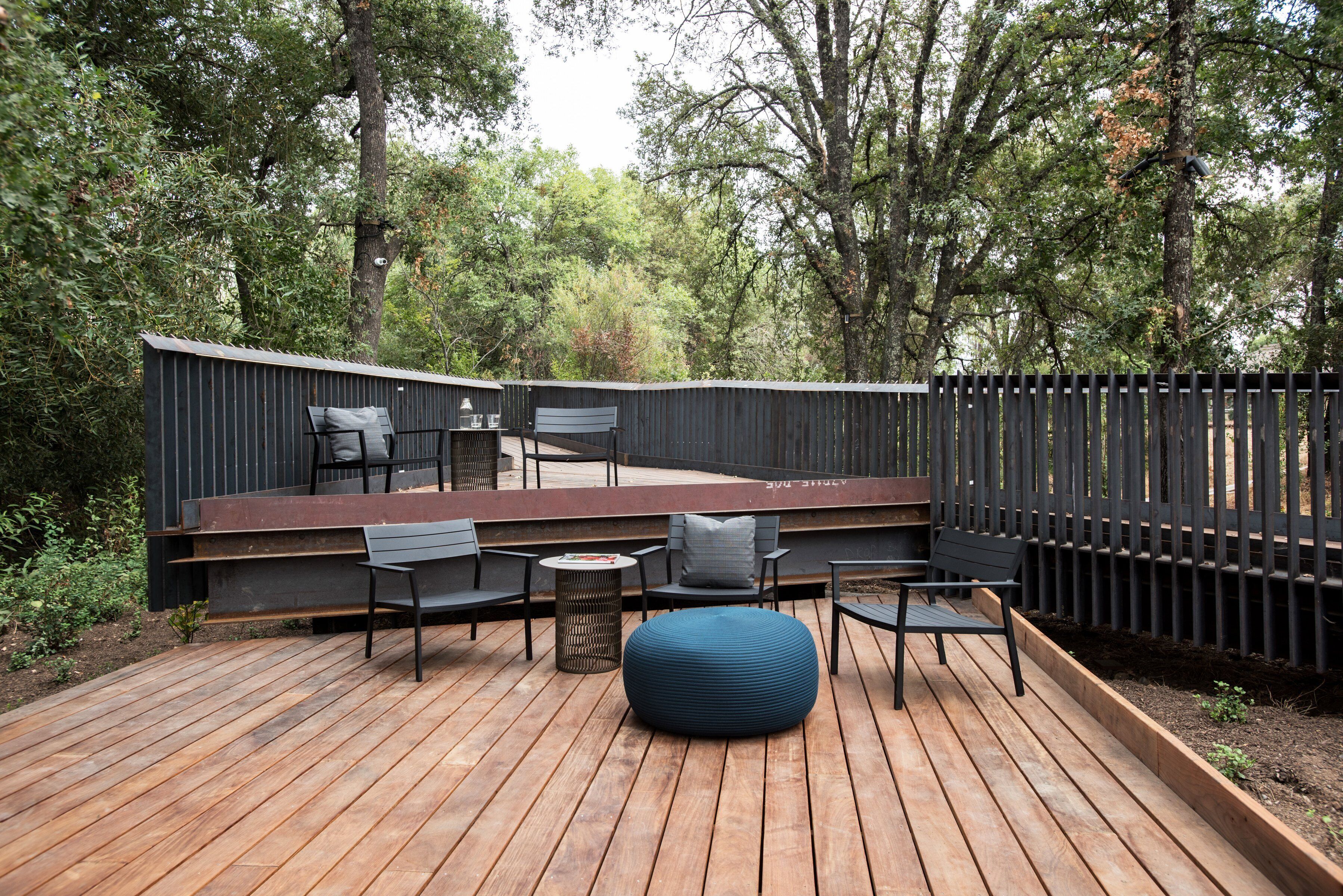 A wooden deck with seating, surrounded by a wooden fence and trees.