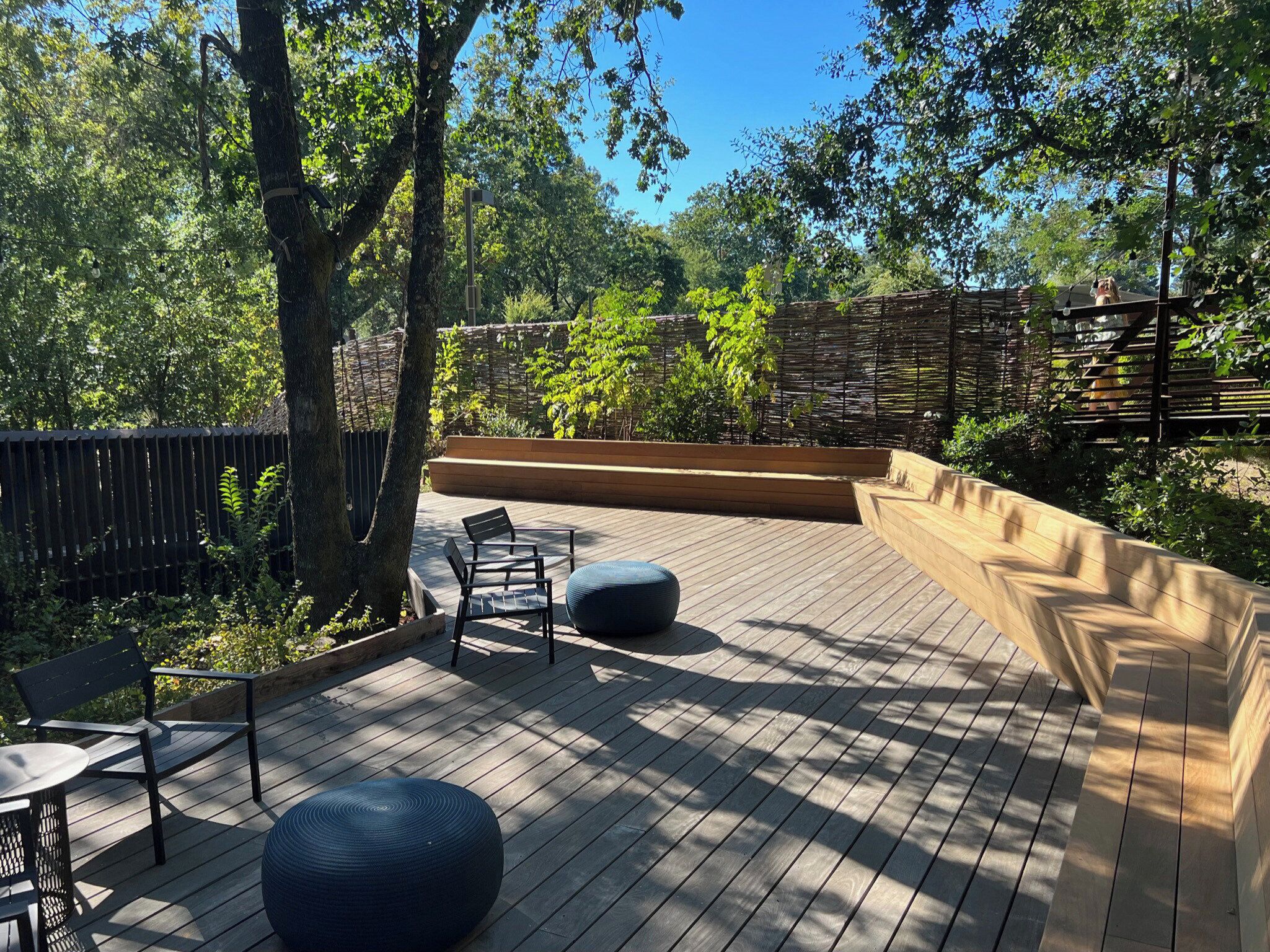 An outdoor deck with wooden flooring, a bench, a table, and a large planter.