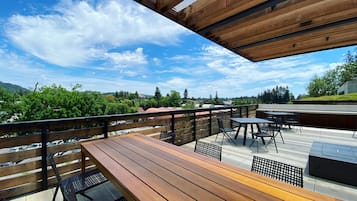 Une terrasse extérieure avec des tables et des chaises en bois, une vue sur un paysage verdoyant et un ciel bleu dégagé.
