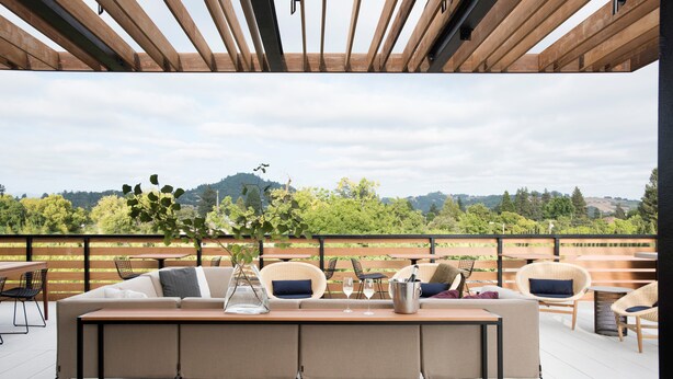 A modern outdoor seating area with a wooden table and chairs, a sofa, and a view of a green landscape. - Harmon Guest House (Healdsburg)
