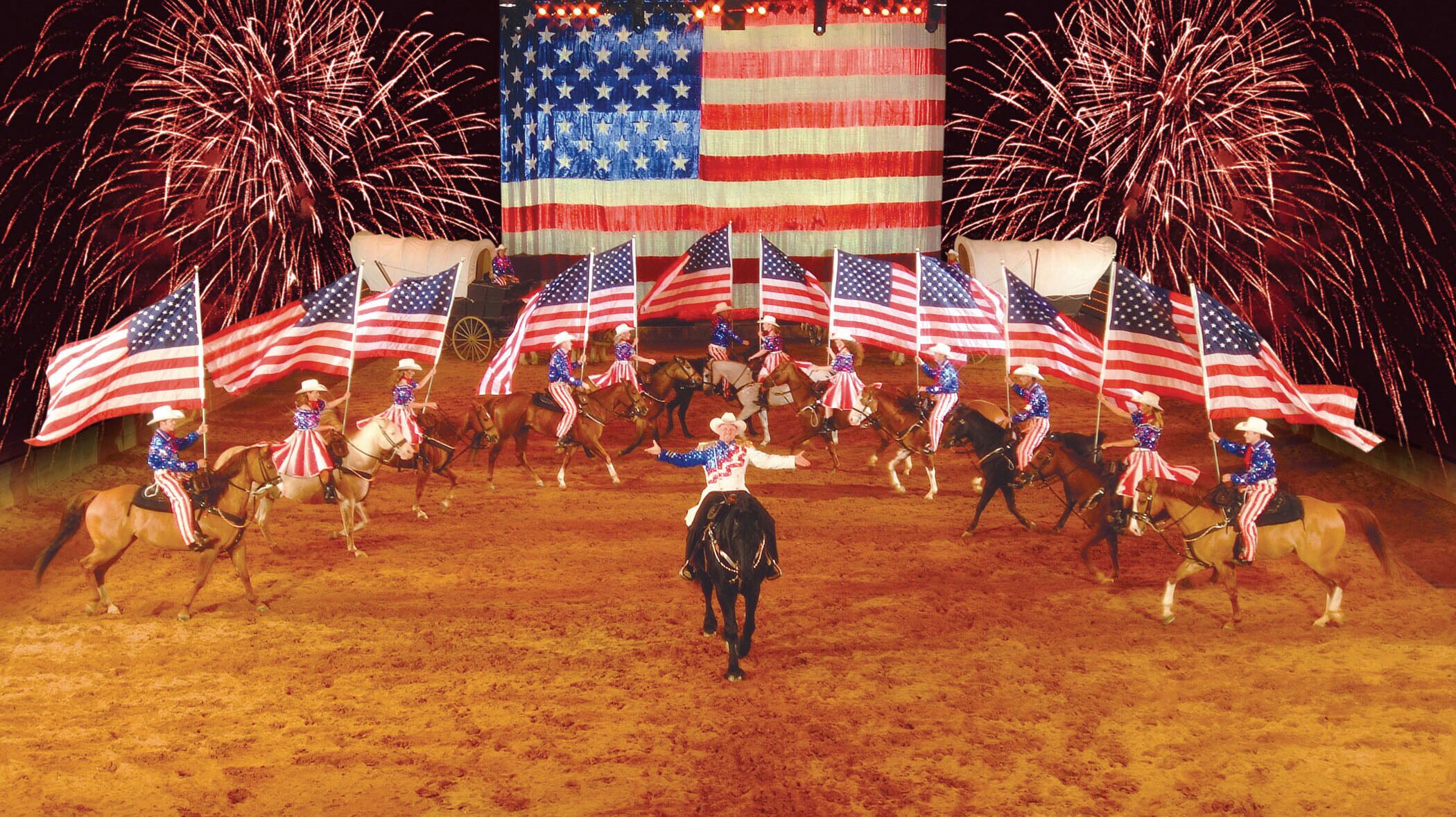 A performance with riders on horses, surrounded by American flags and fireworks.