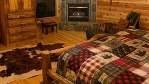 Interior rústico de una cabaña con chimenea de piedra, muebles de madera y un tapete de cuero de vaca.