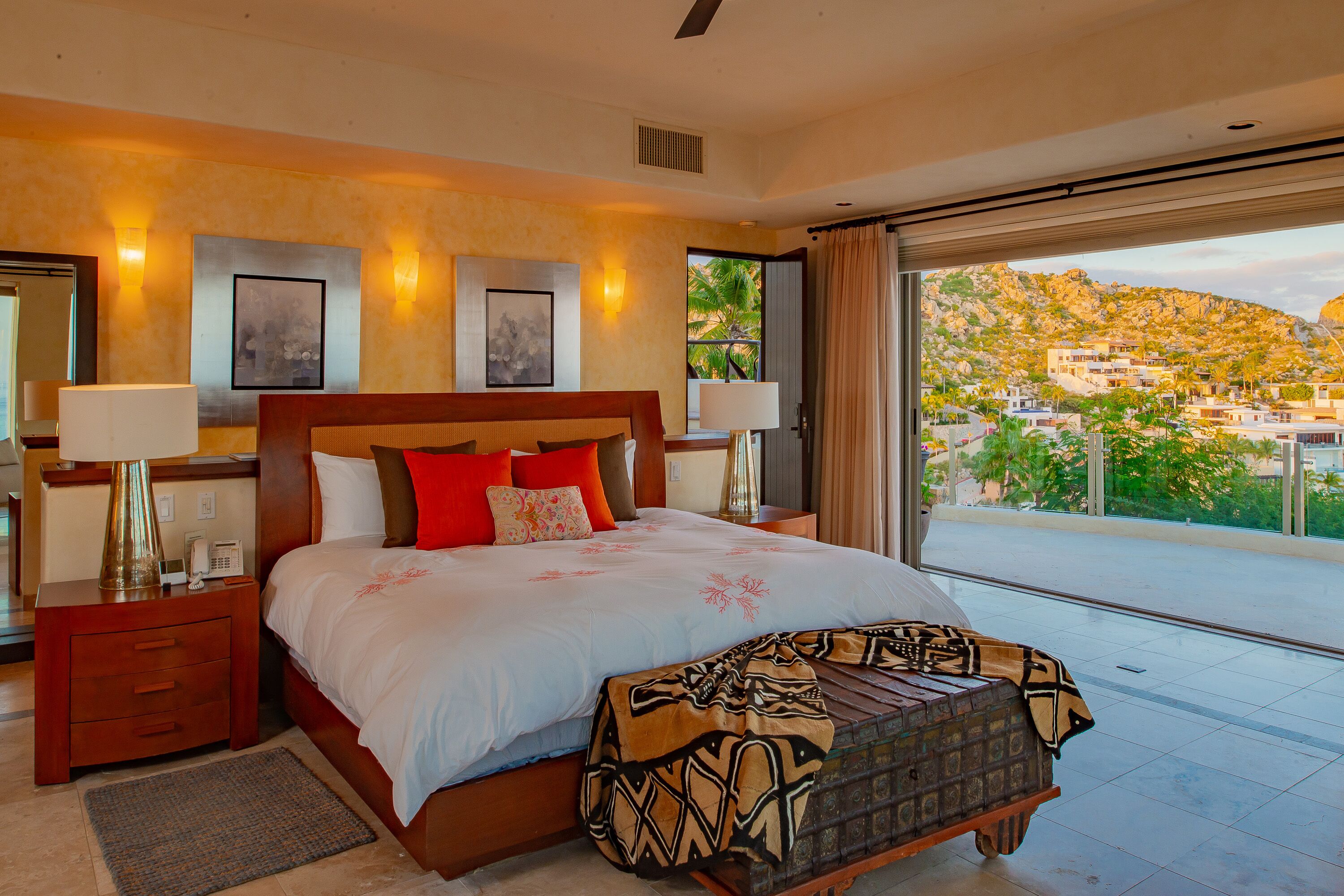Une chambre spacieuse avec un grand lit, deux tables de chevet avec des lampes et une vue sur un paysage montagneux, visible à travers une porte-fenêtre coulissante.