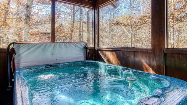Ein Whirlpool in einer Holzhütte mit Holzwänden und großen Fenstern mit Blick auf einen Wald.